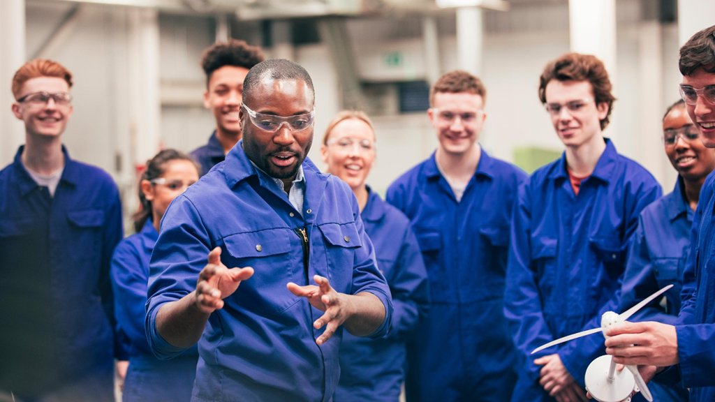 Group of young people learning at an engineering class wearing overalls and safety glasses